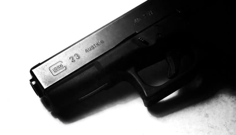 A black handgun half-covered in shadow sits on a white background