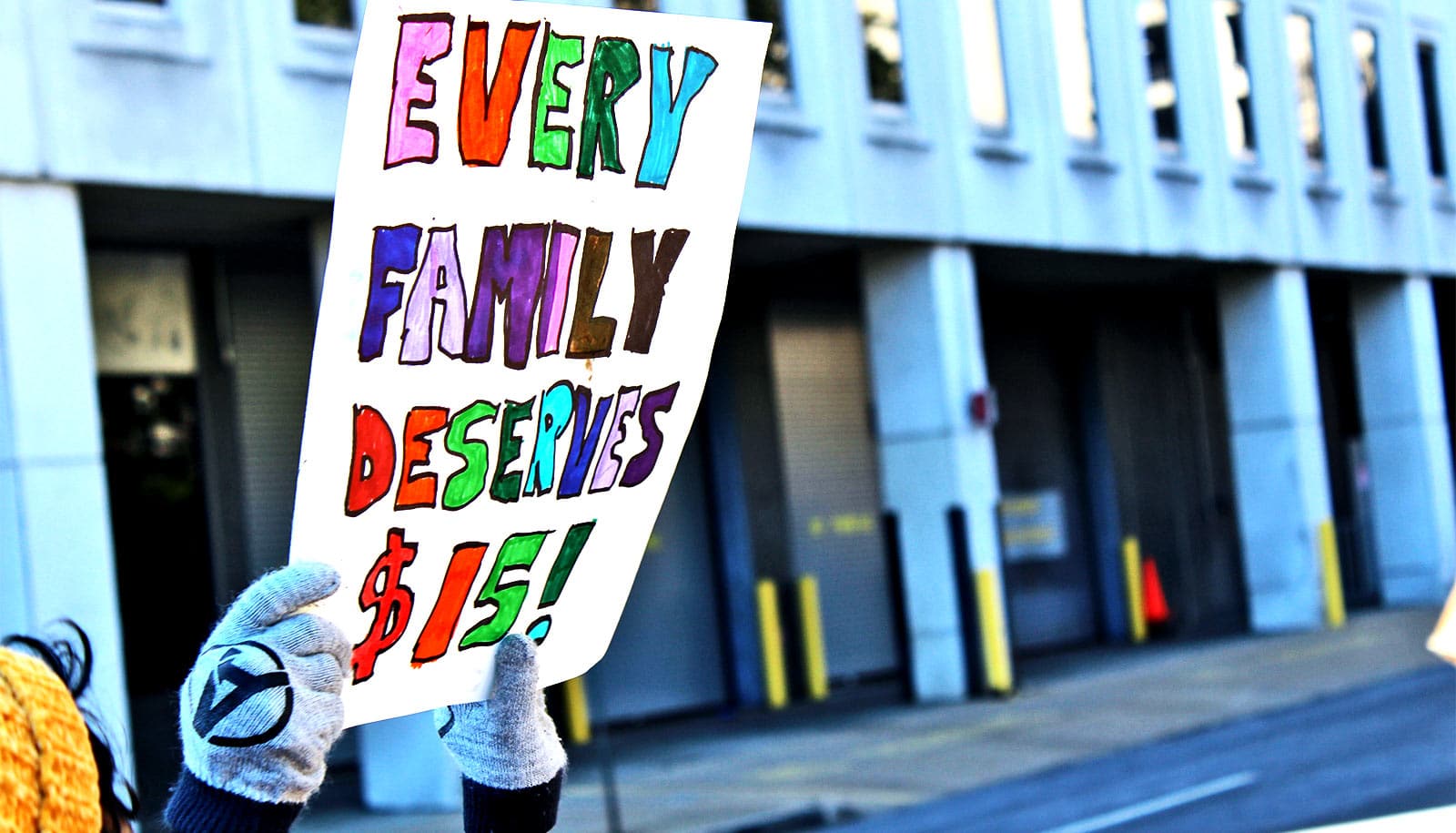 A person holds a sign that reads "Every family deserves $15"