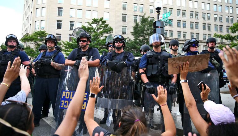 line of police officers behind row of kneeling protestors whose raised hands are visible