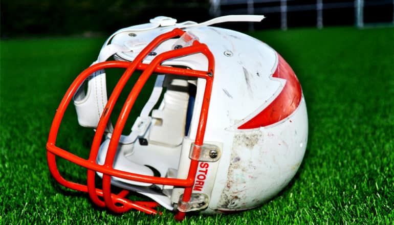 A white and red football helmet lays sideways on green grass