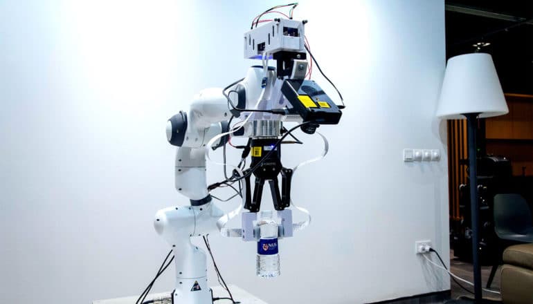 The robot arm holds a water bottle against a white wall