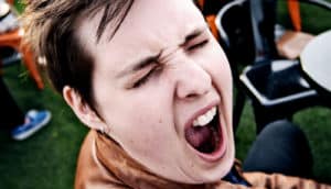 A person sitting at a outdoor dining table yawns with her eyes closed and mouth wide