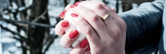 A woman with bright red nails packs a snowball in her hands