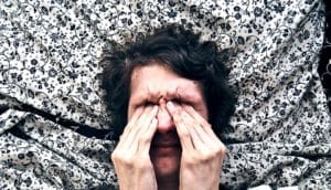 A man rubs his eyes while his head rests on a flowery pillow