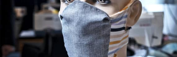 The prototype face mask on a mannequin head. The mask has a gray fabric front section and multi-colored bands of fabric around the back of the head and under the chin
