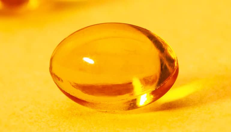 A vitamin D gelcap sits on a yellow/orange background