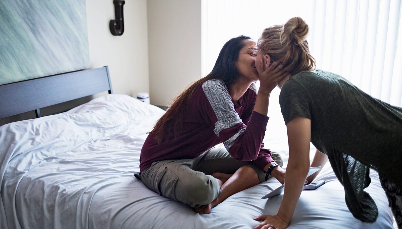 two women kiss on twin bed. 