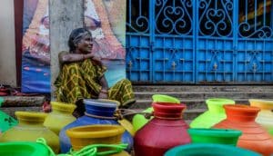 older woman sits behind colorful water jugs