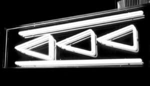 A neon sign looks like a "rewind" symbol of triangles pointed to the left