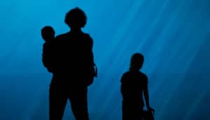 adult holding baby and child in silhouette on blue