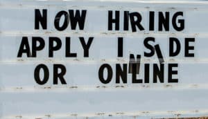 crooked letters on sign read "now hiring apply inside or online"
