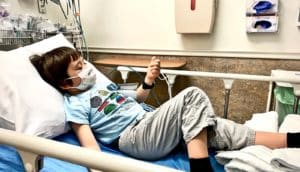 A child lays in a hospital bed wearing a face mask