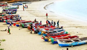 People walk on a beach that also has many boats sitting on the sand