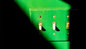 A green wall and light switch in a sliver of light in a dark room