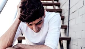 A young man sits on some stairs looking down and leaning on one hand