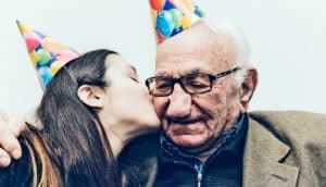A young woman kisses her grandfather, both wearing party hats, on the cheek