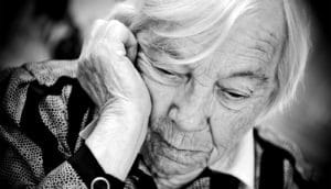 An older woman looks down while touching the side of her head