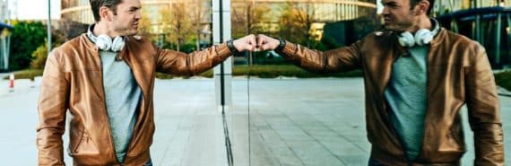 A man fist bumps his own reflection while walking past a large window