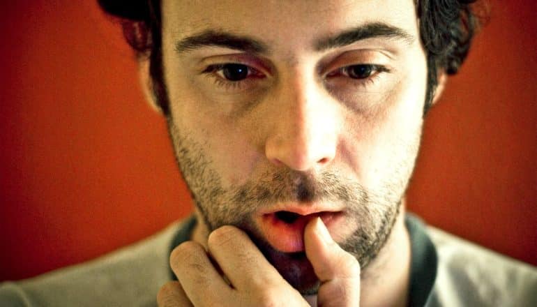 A man looks down and touches his lip while deep in thought