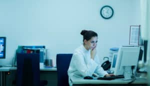 person in white coat looks thoughtfully at computer screen