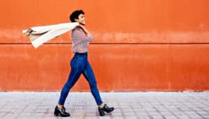 A woman walks past an orange wall tossing her coat over her shoulder
