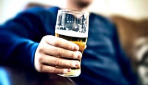 A man sits on a couch while holding a pint glass of beer