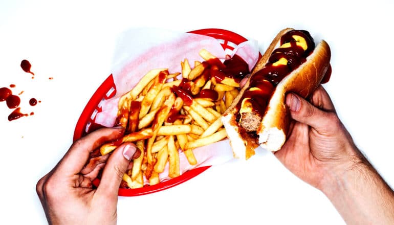 A person eats fries and a hotdog against a white background