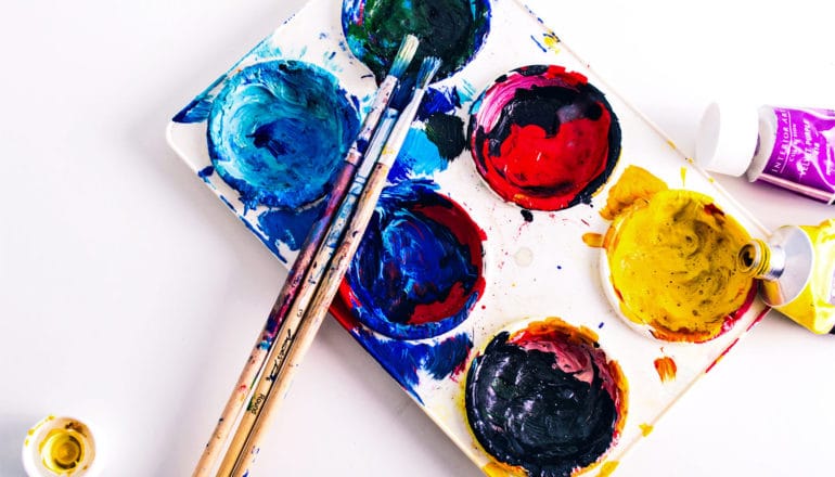 Paintbrushes leaning on a palette with colorful paints