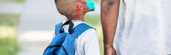 child in mask and backpack looks up at adult and holds hand