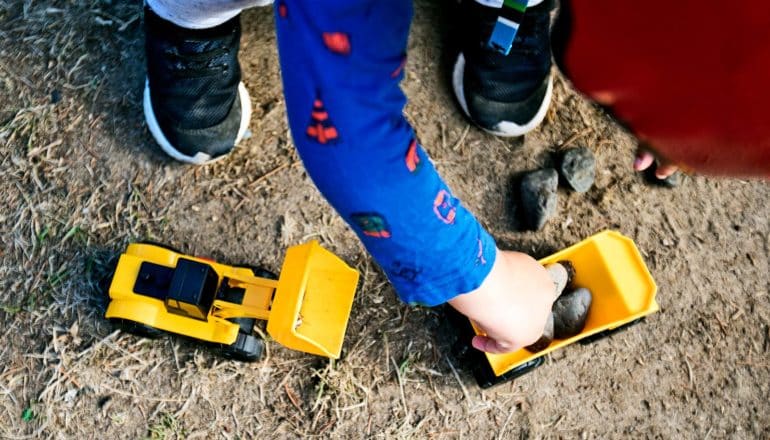A young child plays with yellow toy trucks in the dirt