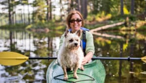 smiling adult in kayak with little dog on the prow