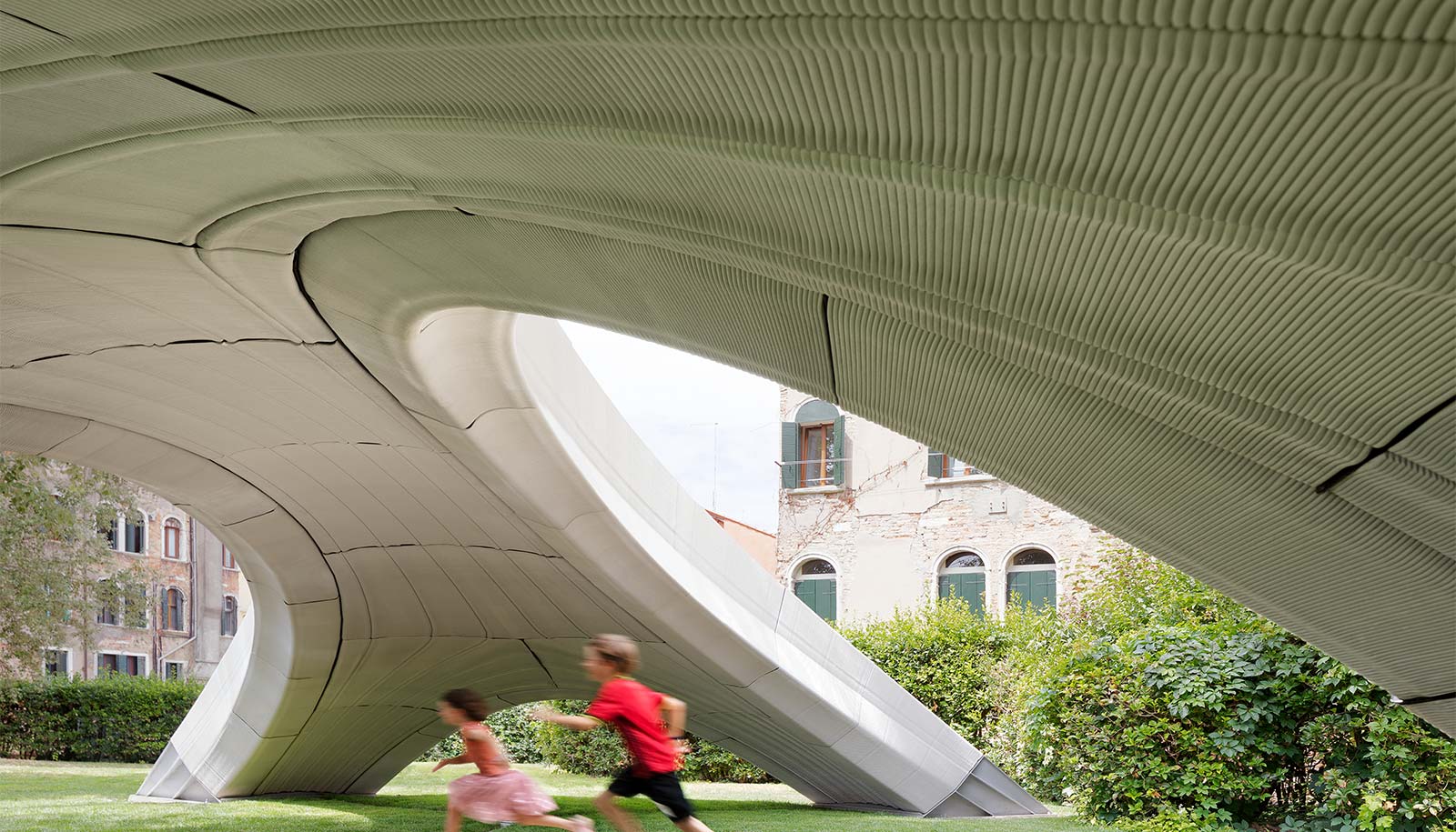 Kids run under the bridge, showing the grooved, curved concrete underneath