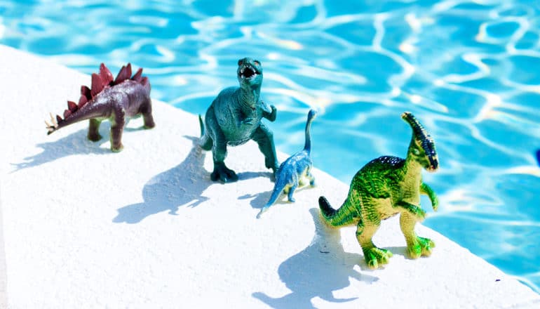 Dinosaurusspeelgoed staat aan de zijkant van een blauw zwembad