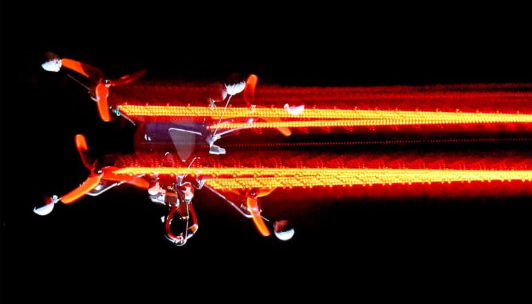 A drone flies fast enough for its lights to blur against a black background
