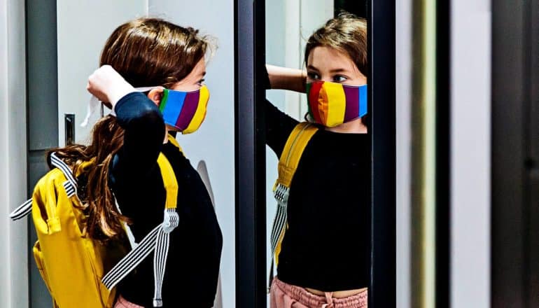 Een jong meisje bindt haar masker vast terwijl ze in de spiegel kijkt terwijl ze zich klaarmaakt voor school