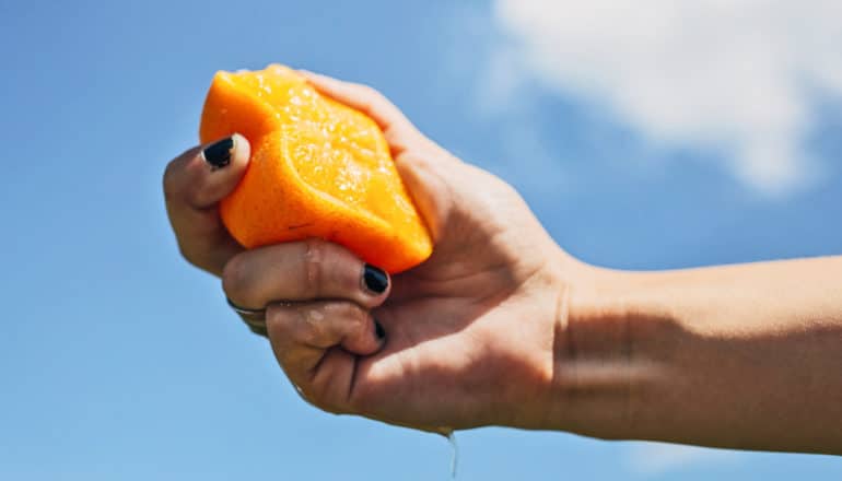 hand squeezes half an orange in front of blue sky