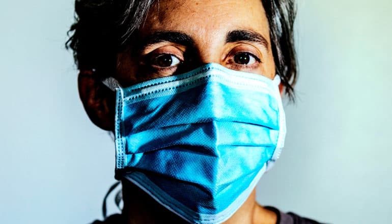 A woman wears a surgical mask while looking at the camera