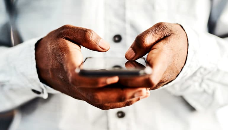 A person in a white button-up shirt holds their phone in two hands