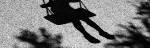 A shadow of a young child on a swing on asphalt