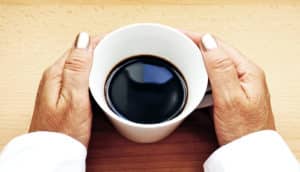A woman holds a cup of coffee in two hands while its on a table