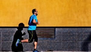 A man runs down the sidewalk against a yellow wall