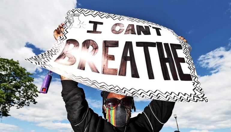 A protestor holds a sign that reads "I can't breathe" against a blue sky