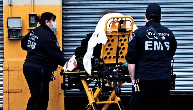 EMS workers wait for a metal door to rise in order to bring a patient on a stretcher into a hospital