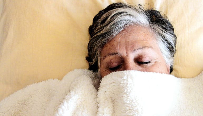 An older woman sleeps with half her face covered by a white blanket