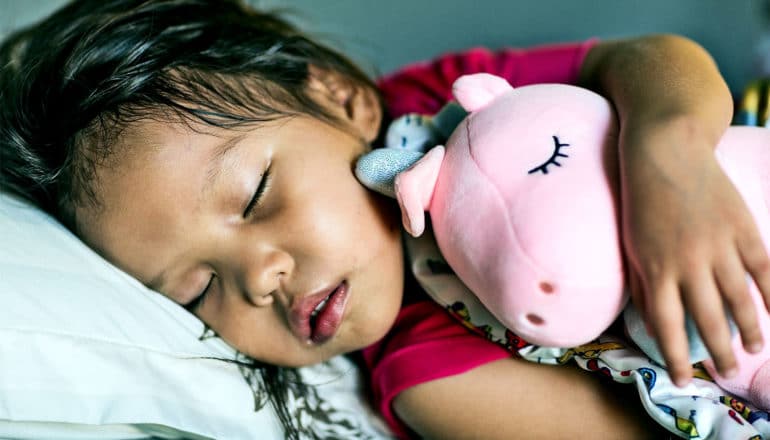 A little girl sleeps with a stuffed unicorn toy