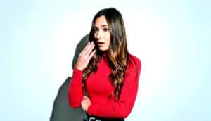 A young woman in red stands alone with her mouth open and hand near her face