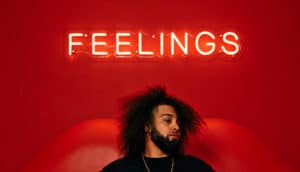 person with beards sits below neon sign that says "FEELINGS"