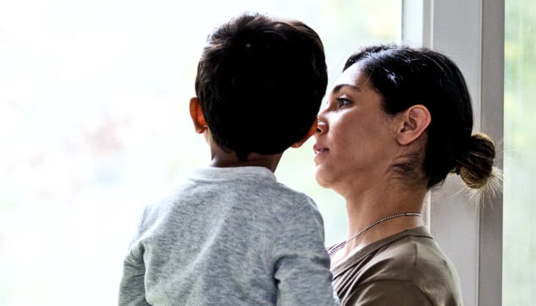 A mother holds her toddler-age son near a window