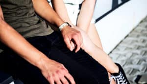 A young couple hold hands while sitting on a short wall