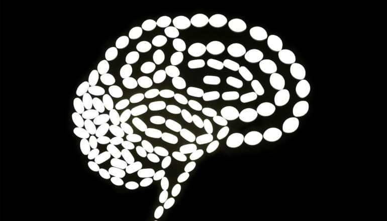 White pills form the shape of a brain on a black background